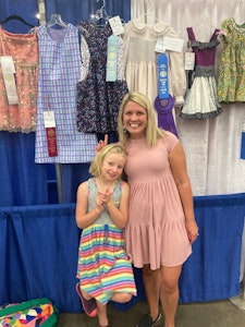 National Craft Month Featured Exhibitor Laura Young and her daughter standing in front of a dress with a red ribbon