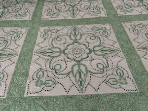 A green and white quilt made with antique embroidery pieces. 